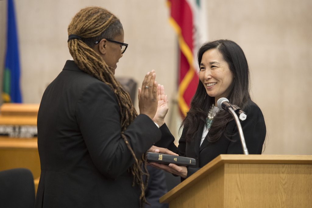 A woman taking an oath while being sworn in by another official during a formal ceremony.