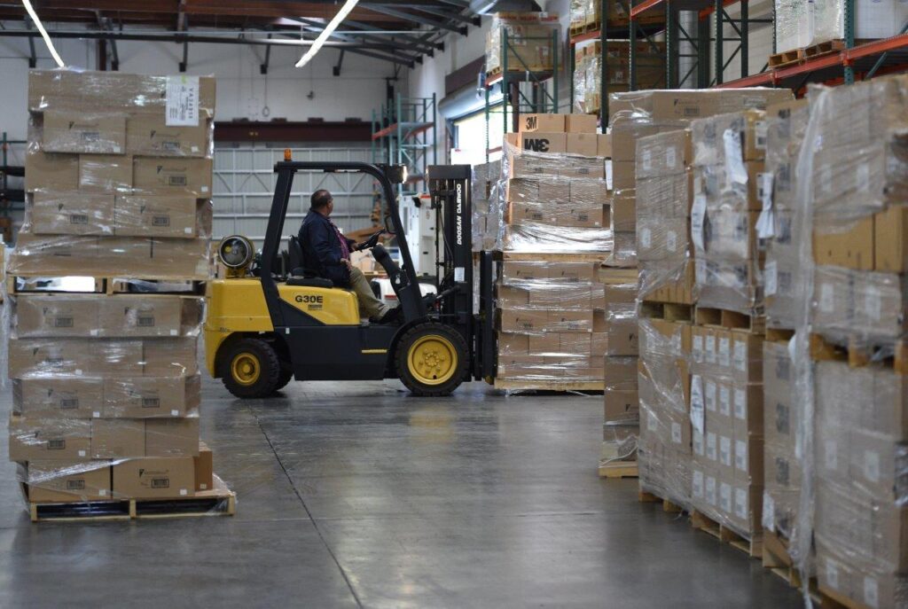 A forklift operator navigating between stacked pallets in a warehouse.