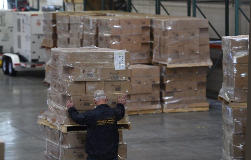 Warehouse worker moving pallets of COVID-19 supplies in a distribution center.
