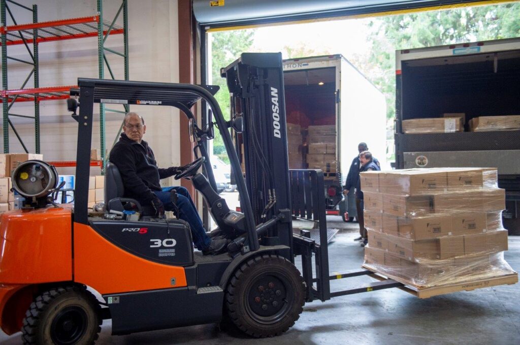 A forklift operator transporting pallets of supplies in a warehouse, supporting COVID-19 relief efforts.