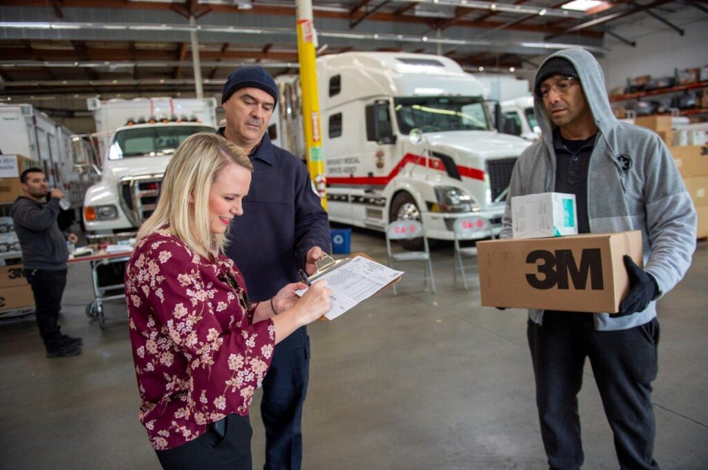 Warehouse staff coordinating the distribution of COVID-19 supplies, with trucks in the background.