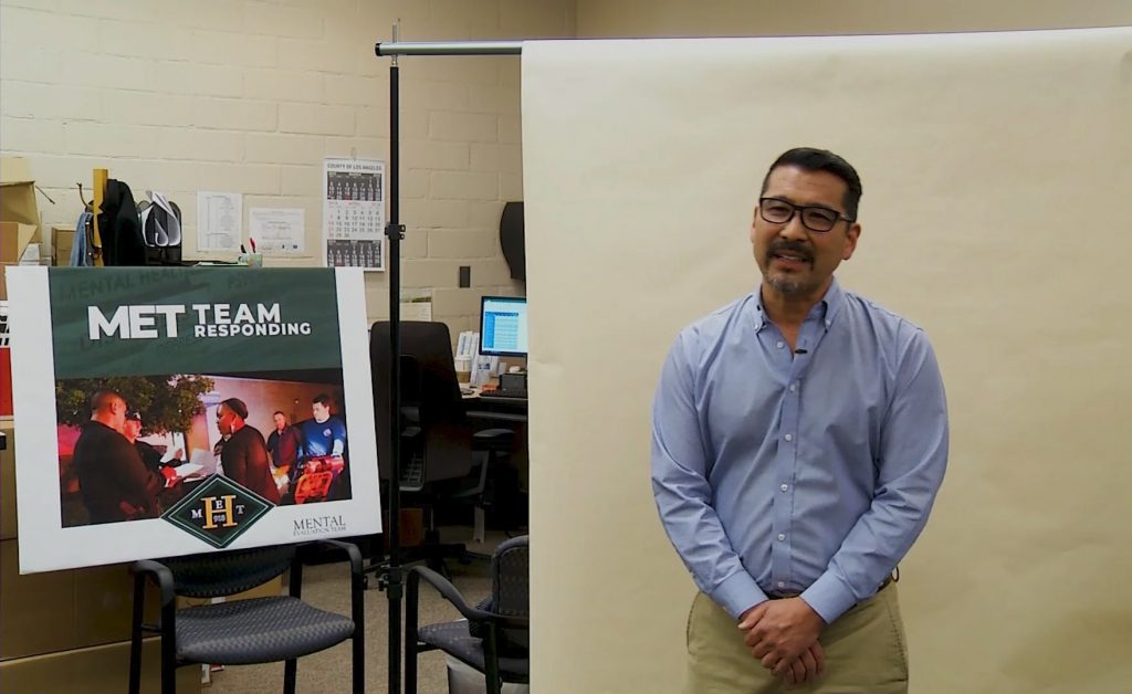 A man stands next to a sign reading "MET TEAM RESPONDING" in a room with office equipment and chairs.