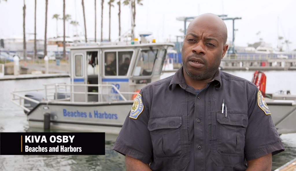 Kiva Osby from Beaches and Harbors speaking at a marina with a service boat in the background.
