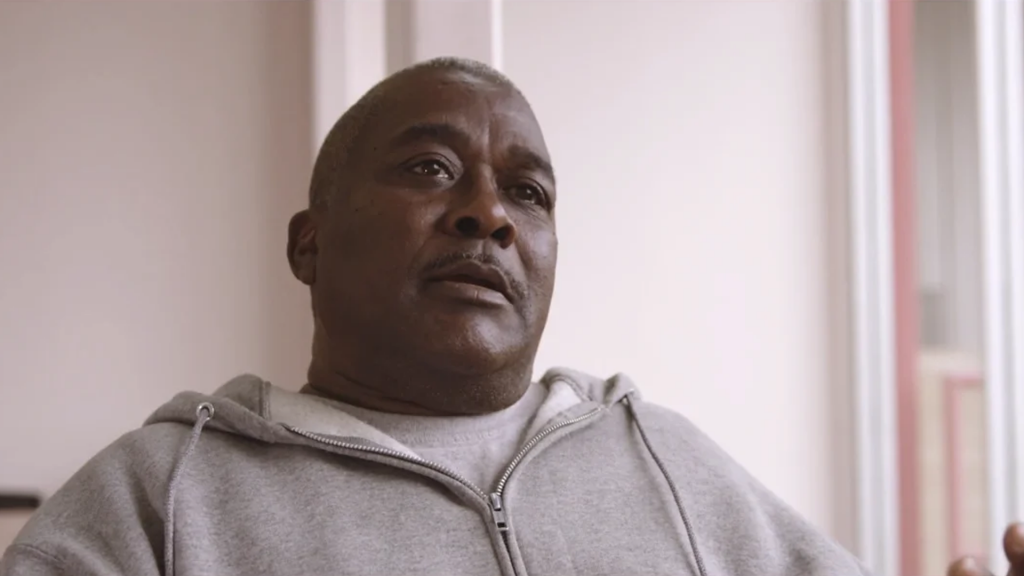 A man in a gray hoodie speaking thoughtfully during a discussion about community health initiatives.
