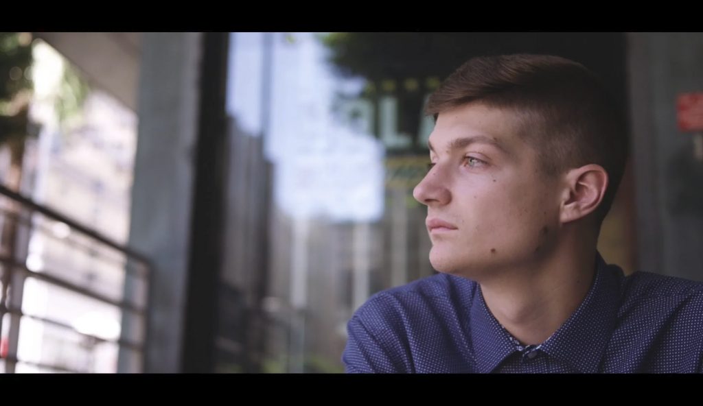 A young man gazes thoughtfully out a window, reflecting on the challenges of the COVID-19 pandemic.