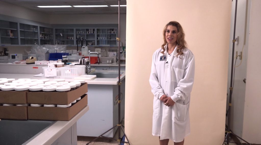 A healthcare professional in a lab coat stands in a laboratory, surrounded by medical supplies and equipment.
